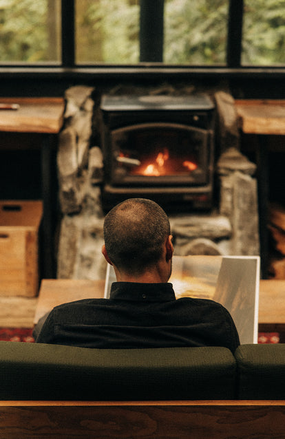 Model sitting and reading by the fireplace.