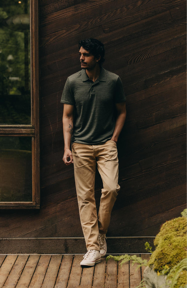 fit model leaning against the wall wearing The Merino Polo in Heather Army