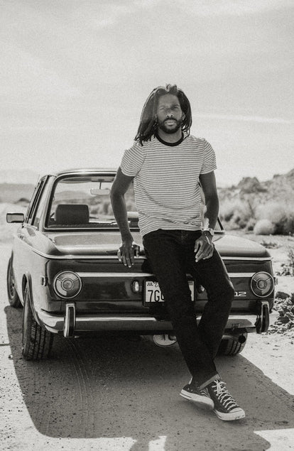 fit model sitting on a car wearing The Cotton Hemp Tee in Black Coffee Stripe