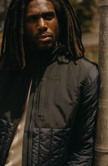 fit model leaning against the wall wearing The Ember Jacket in Dark Navy Quilted Nylon