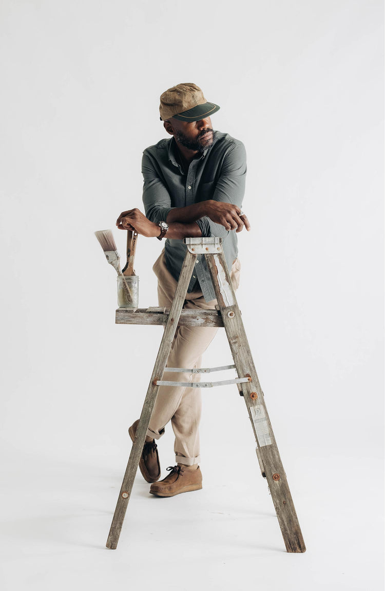 fit model leaning against a ladder wearing The Carmel Pant in Heather Khaki Cotton Linen