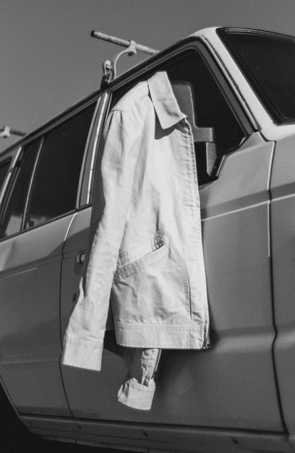 editorial image of The Shifter Jacket in Stone Pigment Canvas hanging on a car