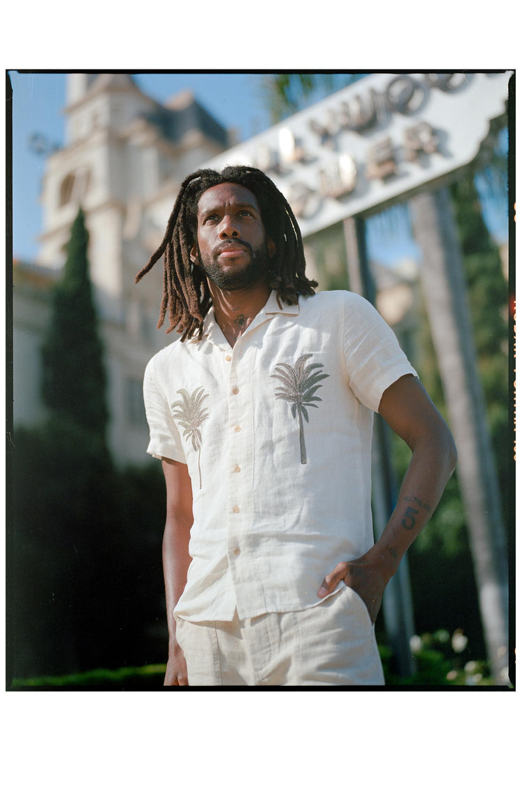 fit model posing in front of a sign wearing The Short Sleeve Davis Shirt in Natural Palm Embroidery