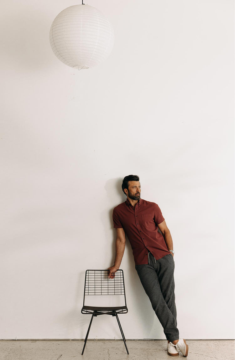 fit model leaning on a chair wearing The Short Sleeve Jack in Dried Cherry Seersucker