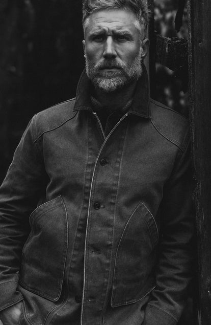 fit model leaning against the wall wearing The Upland Jacket in Aged Penny Chipped Canvas