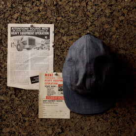 editorial image of The 5-Panel Cap in Washed Indigo hanging on a corkboard, Accessories by Taylor Stitch