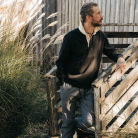 fit model leaning against the wall wearing The Rugby Shirt in Coal, Knits by Taylor Stitch