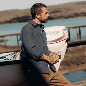 fit model leaning against a boat wearing The Utility Shirt in Indigo Ash Wool Canvas, Wovens by Taylor Stitch