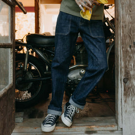 fit model leaning against the wall wearing The Mariner Jean in Rinse Organic Selvedge, Bottoms by Taylor Stitch