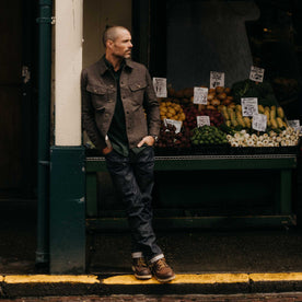 fit model leaning against the wall wearing The Democratic Jean in Rigid Organic Selvedge, Bottoms by Taylor Stitch