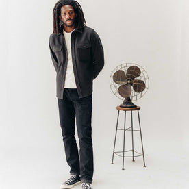 fit model posing next to a fan wearing The Maritime Shirt Jacket in Faded Black Moleskin Twill, Outerwear by Taylor Stitch