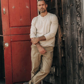 fit model leaning against the wall wearing The Organic Cotton Henley in Heather Oat, Knits by Taylor Stitch