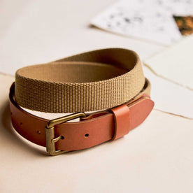 editorial image of The Webbed Belt in Whiskey rolled up on pieces of paper, Accessories by Taylor Stitch