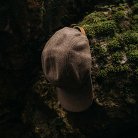 editorial image of The 5-Panel Cap in Heather Sable Wool Blend on a rock, Accessories by Taylor Stitch