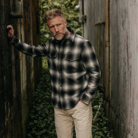 fit model leaning on the wall wearing The Maritime Shirt Jacket in Olive Plaid, Wovens by Taylor Stitch