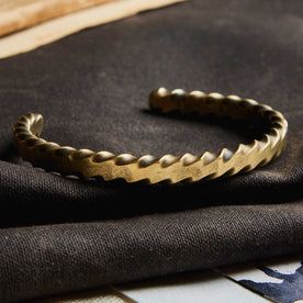 editorial image of The Twisted Cuff in Brass on a piece of fabric, Accessories by Taylor Stitch