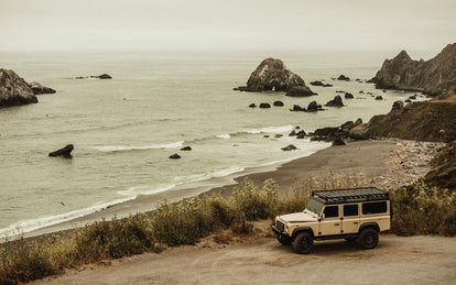 Landrover parked in a pull-out overlooking a rocky bay.