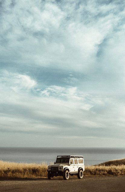 Landrover parked at the side of a road overlooking the ocean.