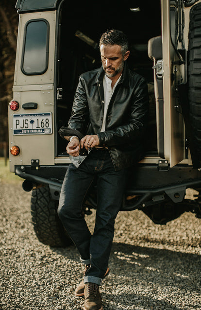 Rolling up the cuff on a leather jacket, sitting on the back step of a Landrover.