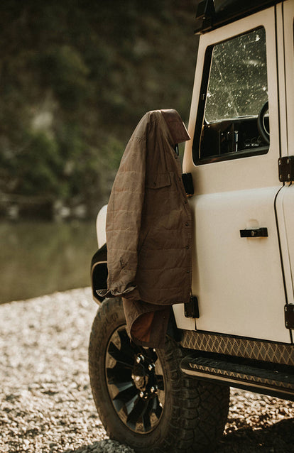 A jacket hung on the side view mirror of a white Landrover.