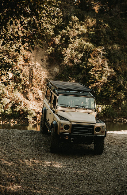 A Landrover driving over a stony bank, coming away from a river.