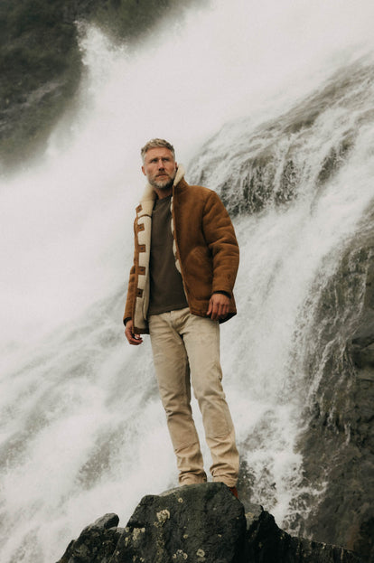 Model standing in front of a waterfall, wearing The High Plains Coat